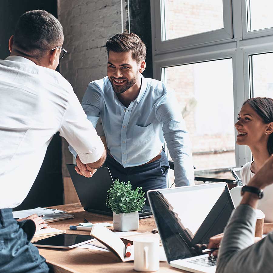 Young modern men in smart casual wear shaking hands and smiling while working in the creative office